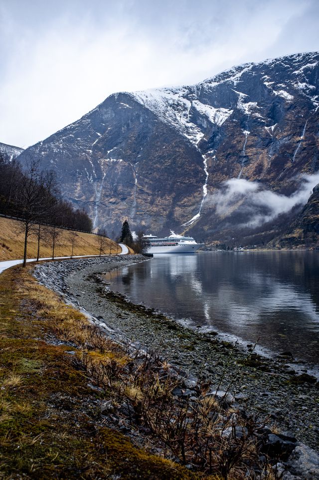 Rocky beach leading to cruise ship, with frozen waterfall spiral up in the background